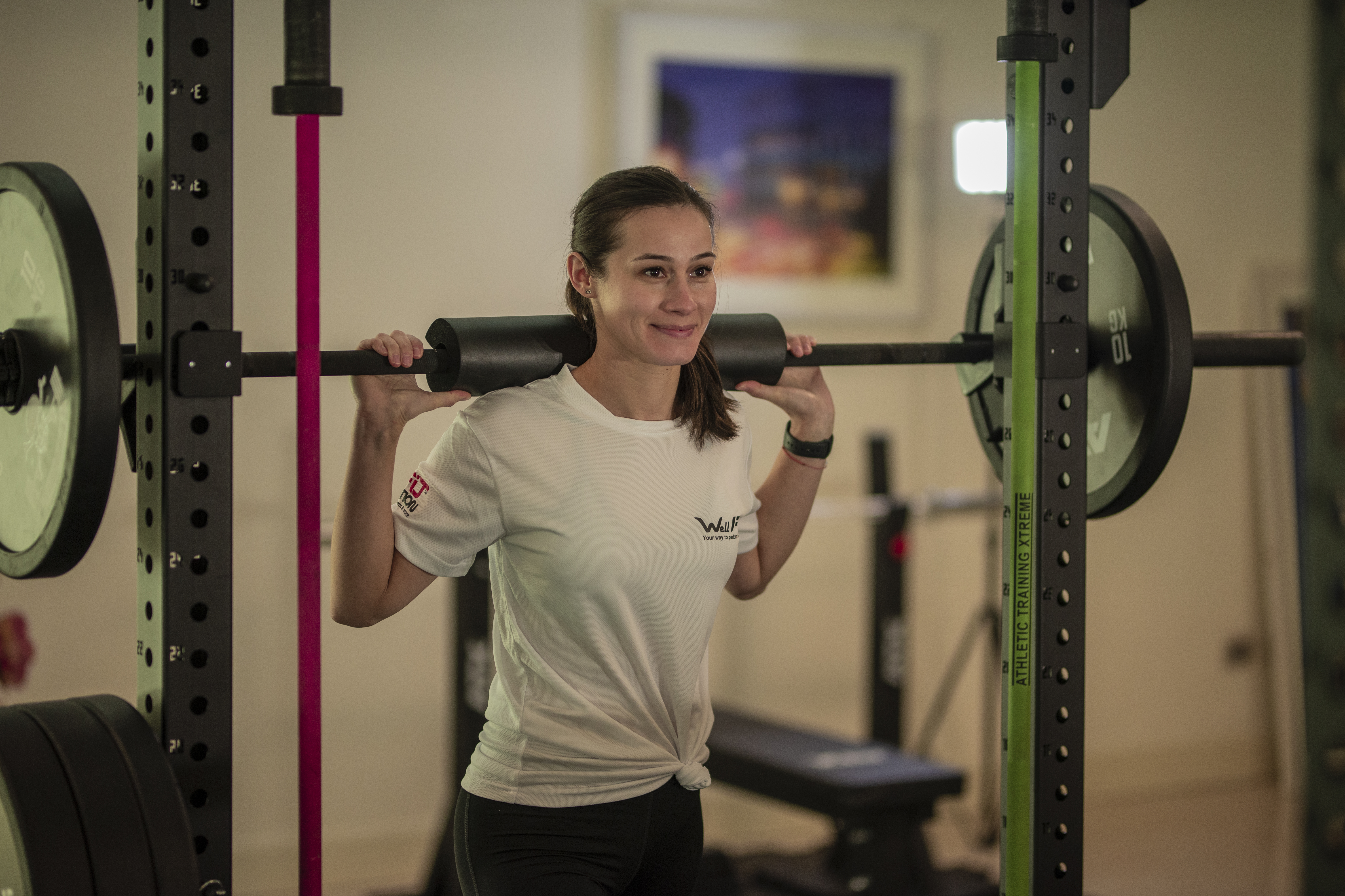 Femeie care se antreneaza in sala cu bara olimpica